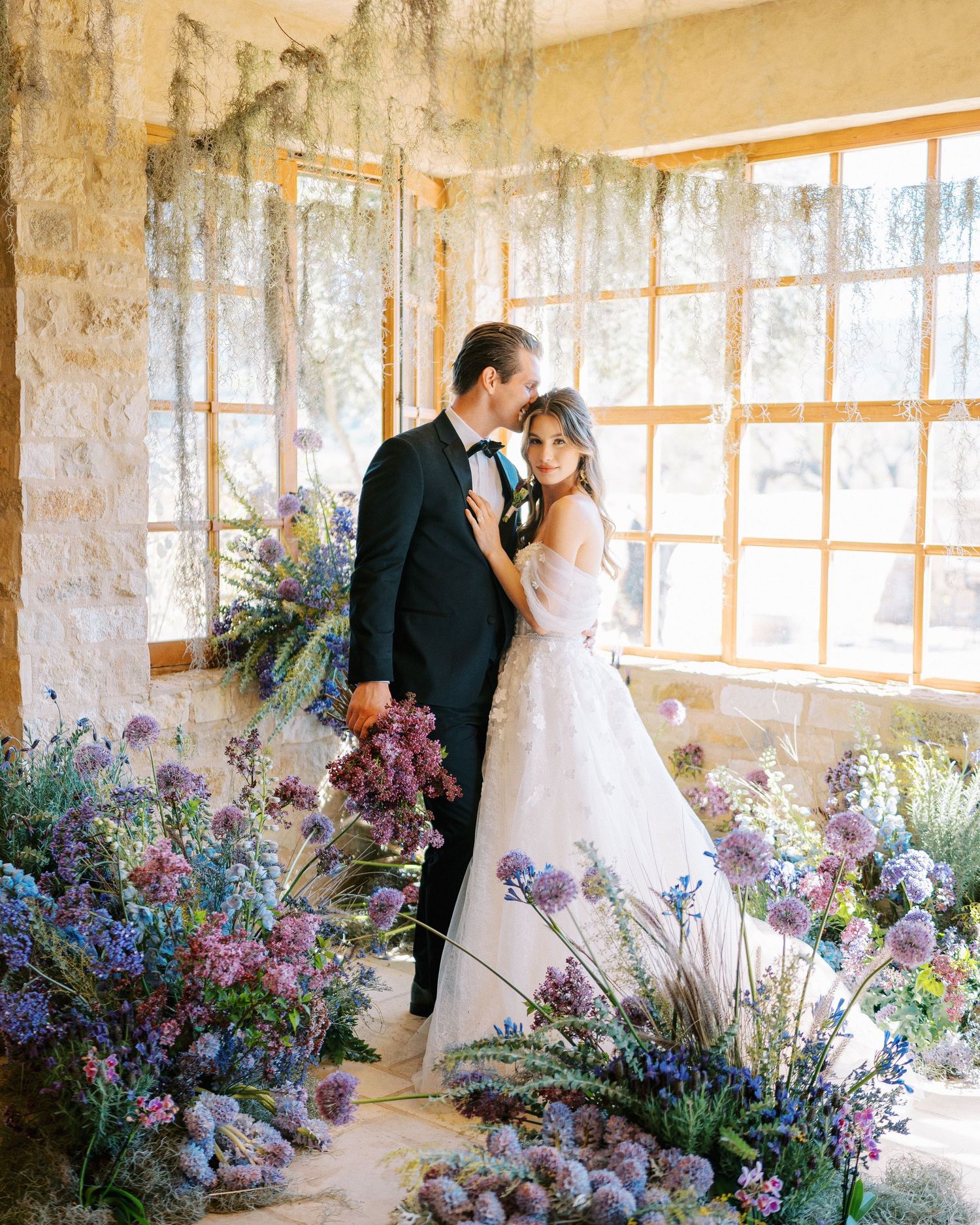 A wedding scene with delicate purple flowers decorating a rustic stone room.