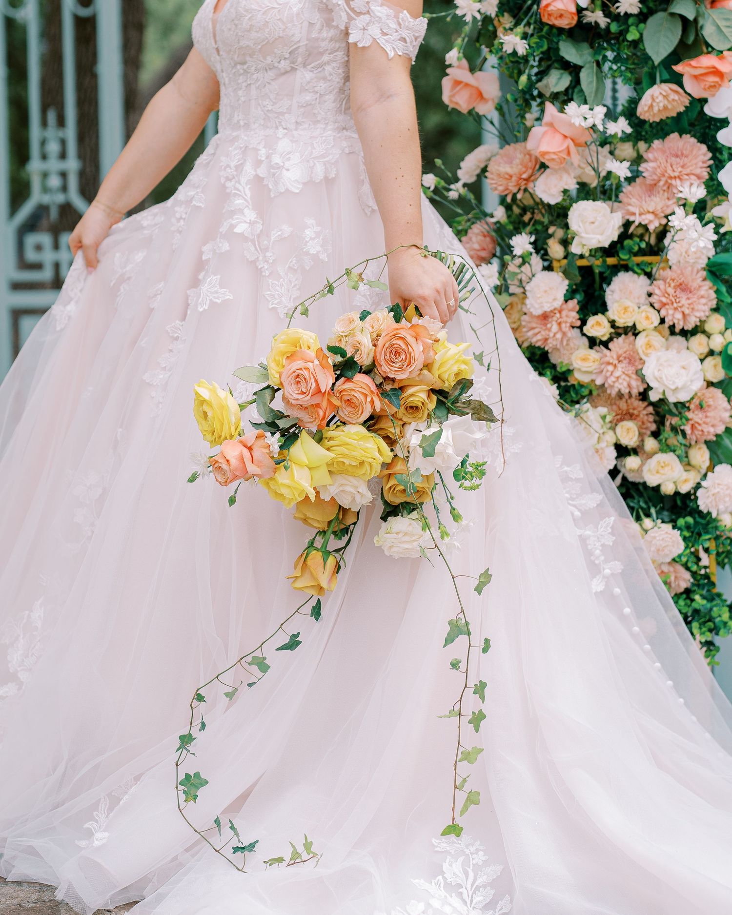 Close-up of a pink wedding dress with peach and yellow floral bouquet.