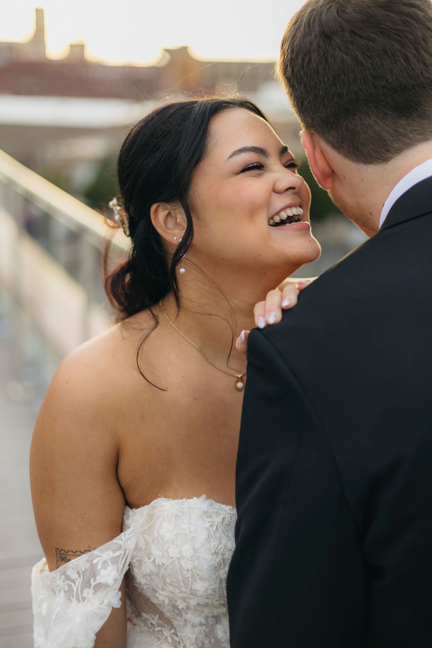 A bride in a strapless lace wedding dress laughs joyfully during an intimate moment with her partner.