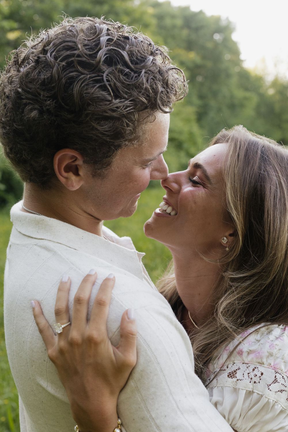 A joyful couple shares a romantic nose-to-nose moment outdoors, with the woman wearing an engagement ring.