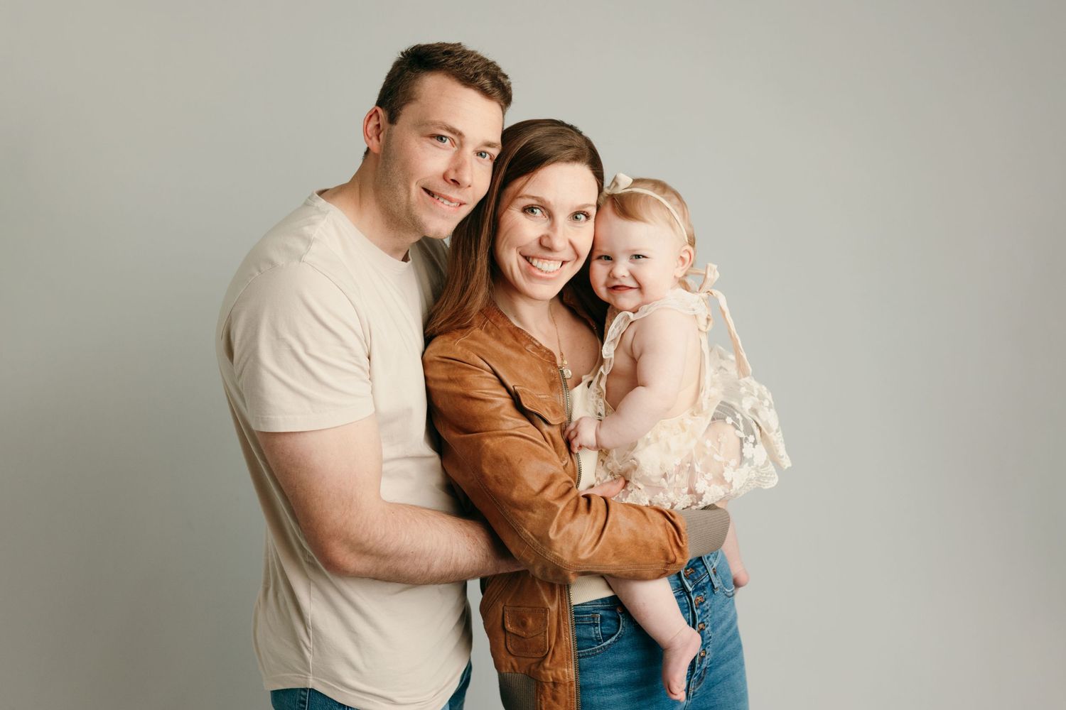 A family of three poses together against a dark brown backdrop at the professional studio in Victoria BC.