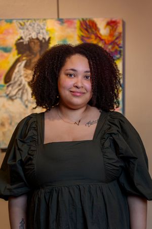 Person in a black dress with puff sleeves poses in front of colorful abstract artwork in a gallery.
