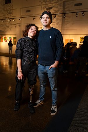 People's lower bodies and feet shown walking through a dimly lit art gallery exhibition space.