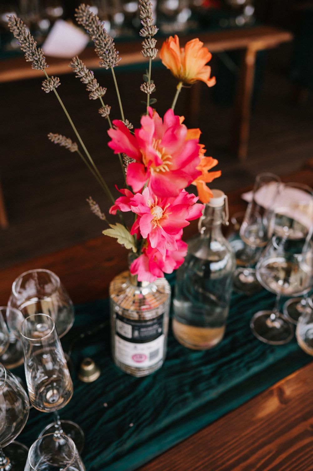 Elegant table setting with bright pink tropical flowers and glass stemware on a dark teal velvet runner.