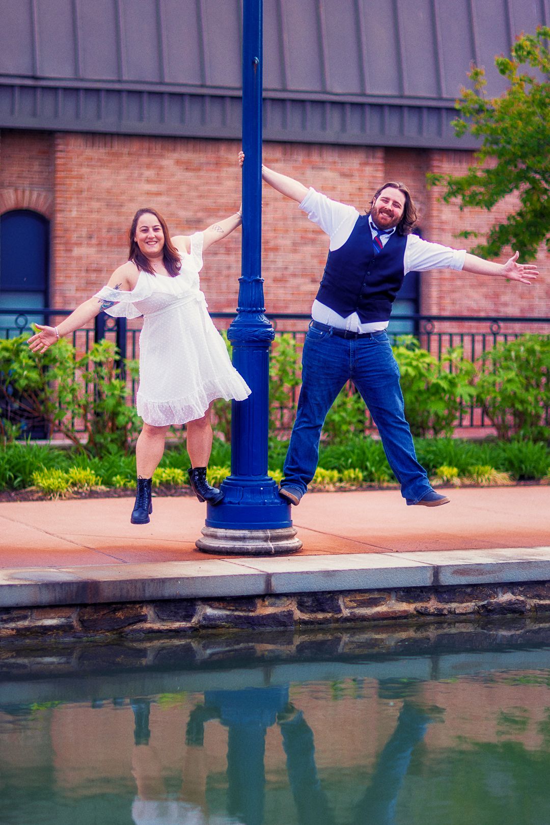 A couple in formal attire playfully pose near a waterfront brick building in a creative photo sequence.