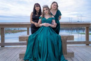Three women in elegant emerald green dresses pose together for prom photos on a wooden deck overlooking a waterfront in Charleston, SC.