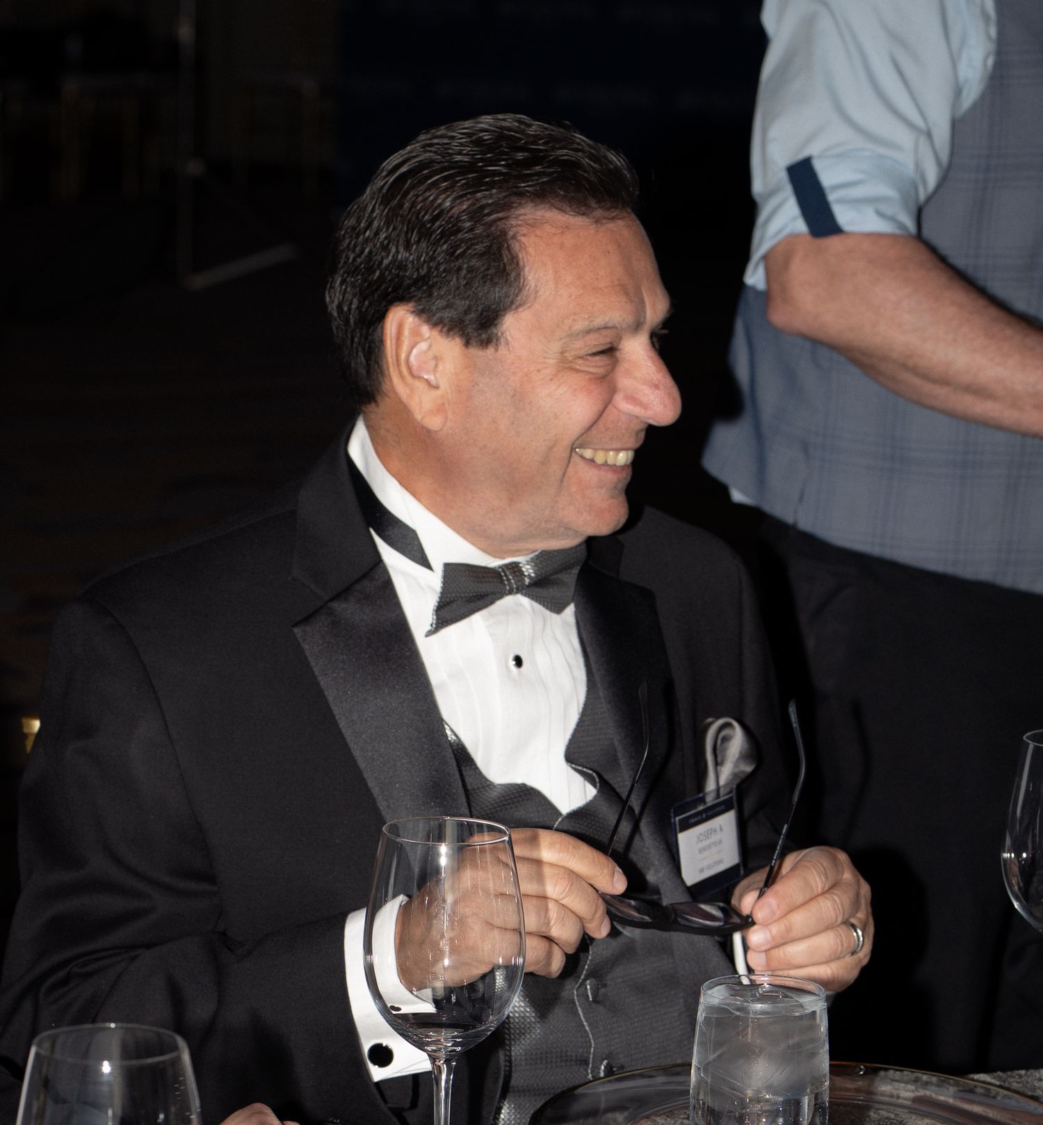 People in black tie attire seated at dining tables during an evening gala event.