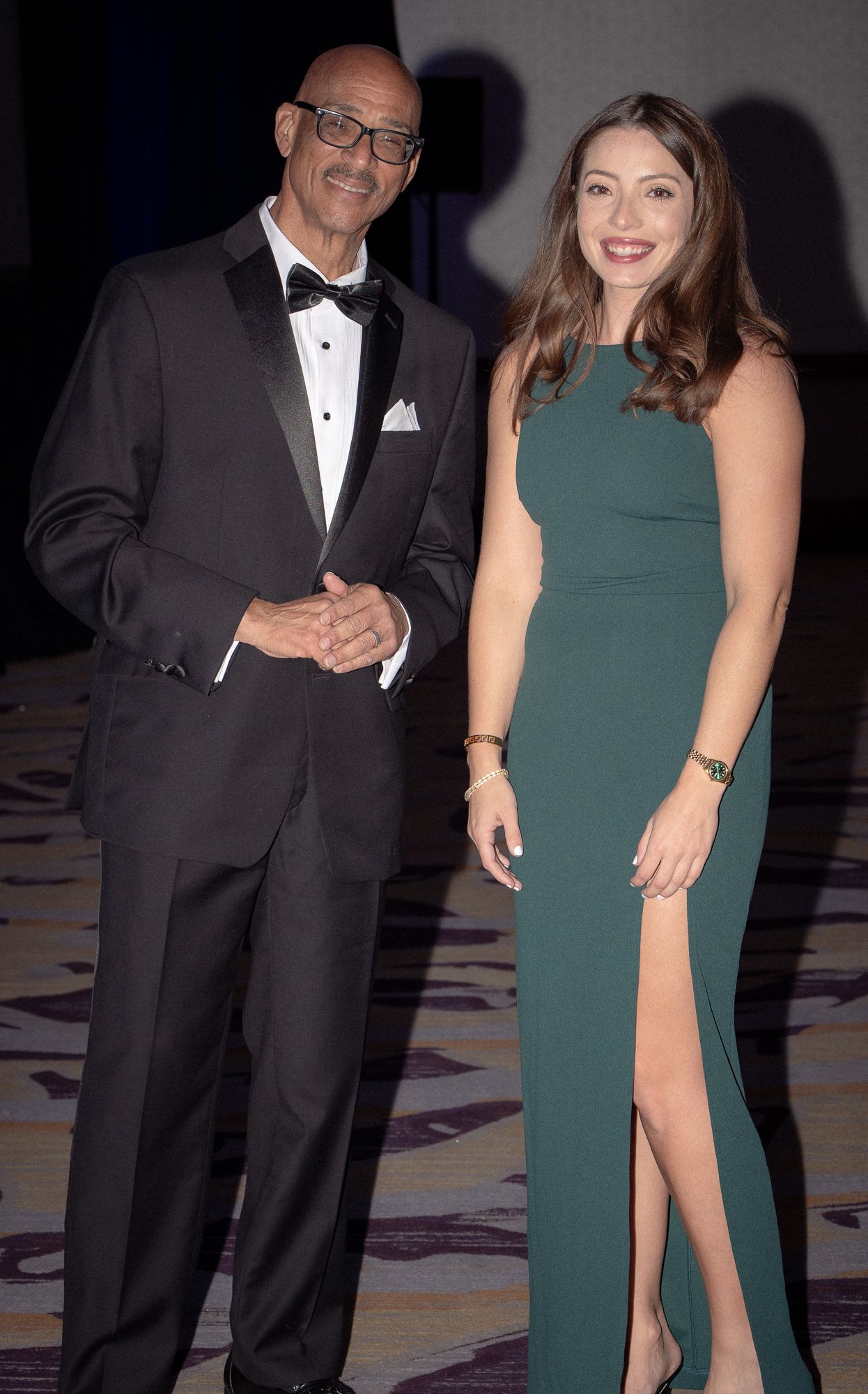 Guests in formal attire including tuxedos and an emerald dress pose at an elegant evening event.