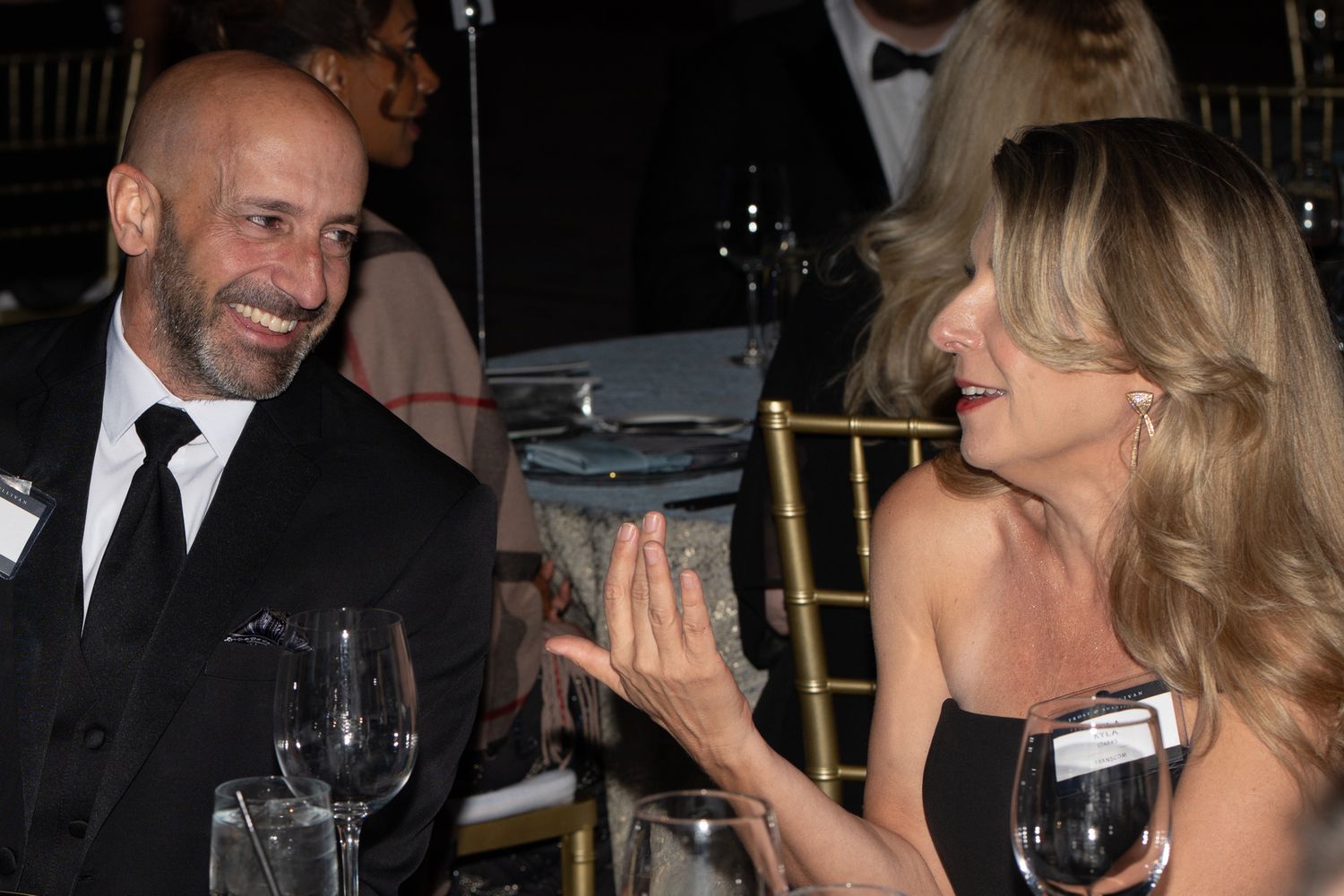 A group of formally dressed people laughing and socializing at an elegant evening event.