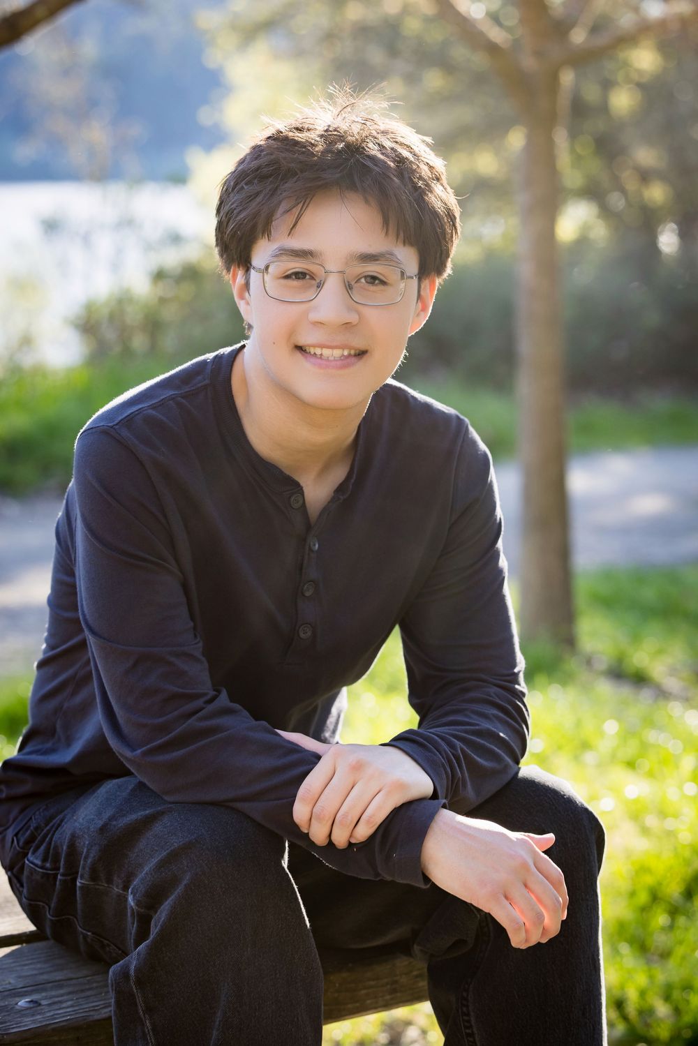 Portrait photos of someone in a navy shirt sitting outdoors with sunlit grass and trees in the background.