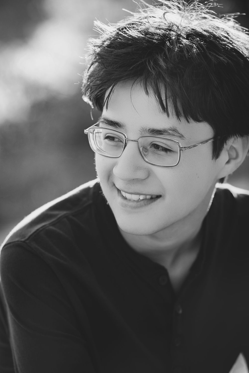 Black and white portrait of a young person with glasses smiling while wearing a dark shirt.