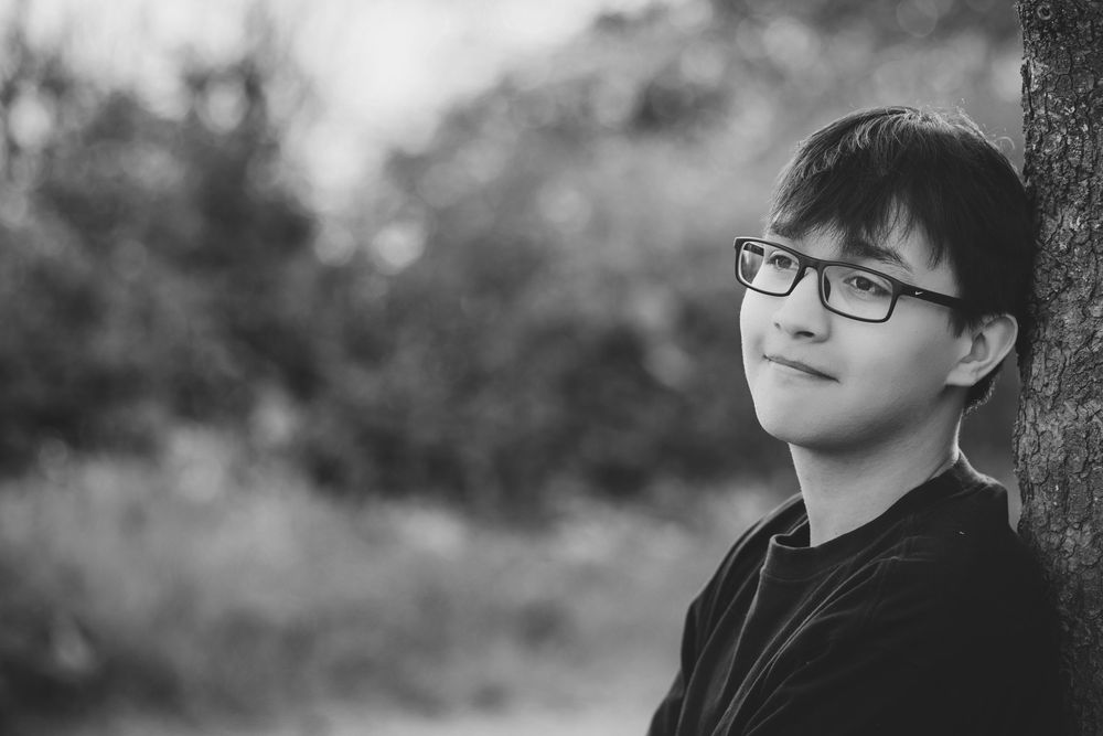 A series of black and white portraits showing a person wearing glasses leaning against a tree in different poses.