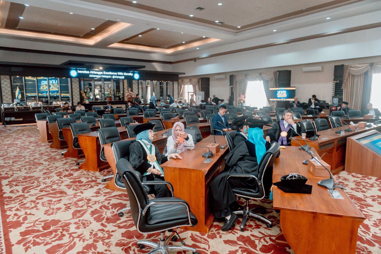 Wide panoramic view of a modern university auditorium with blue seats and wooden podium stage.