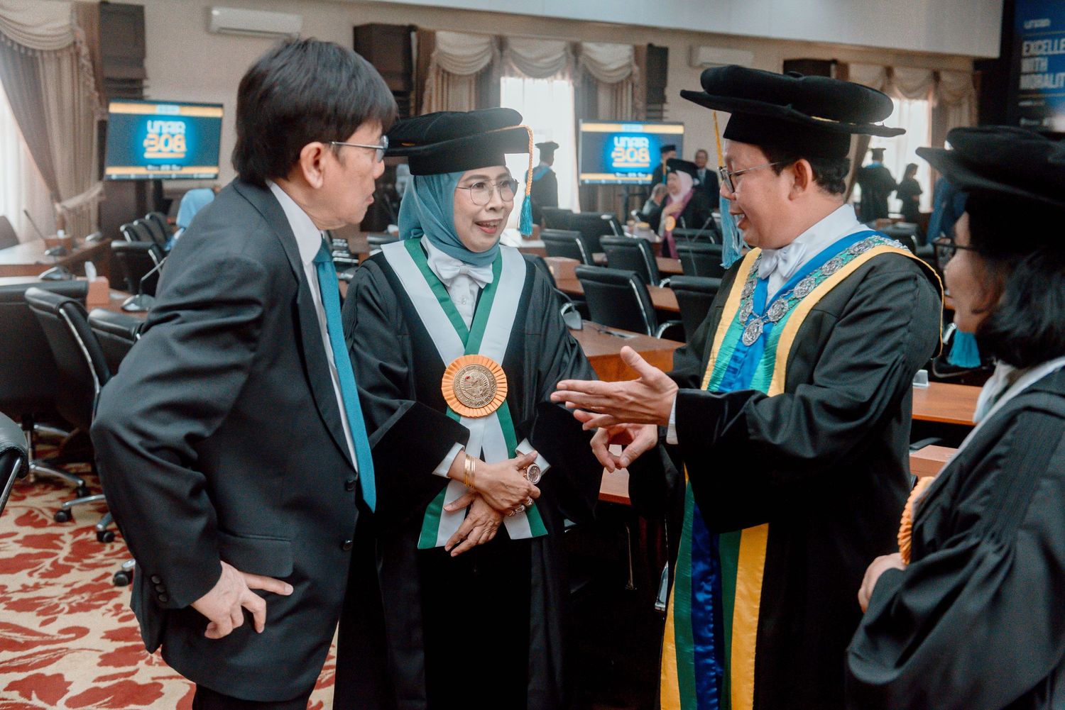 A group of graduates in academic regalia interact enthusiastically during a graduation ceremony.