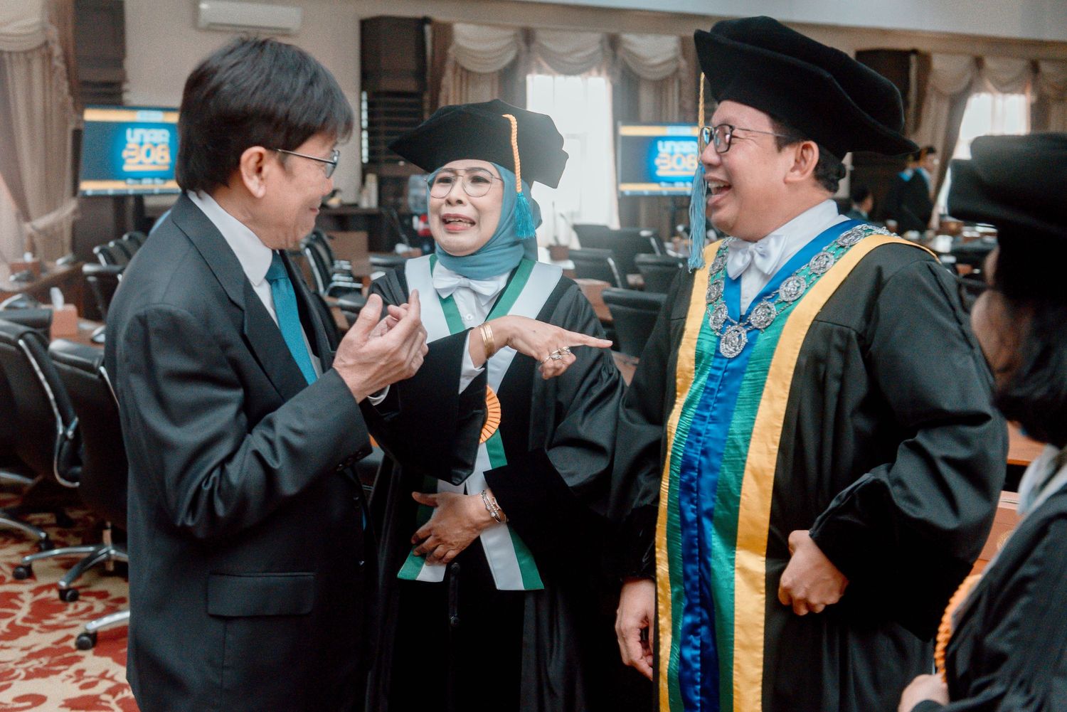 Three people in academic regalia having an animated conversation during a graduation ceremony.