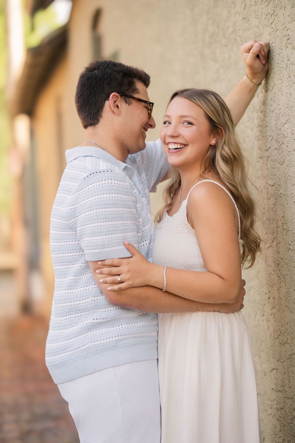 A couple in white outfits embraces and laughs together during an outdoor engagement photo session. German Village Engagement session