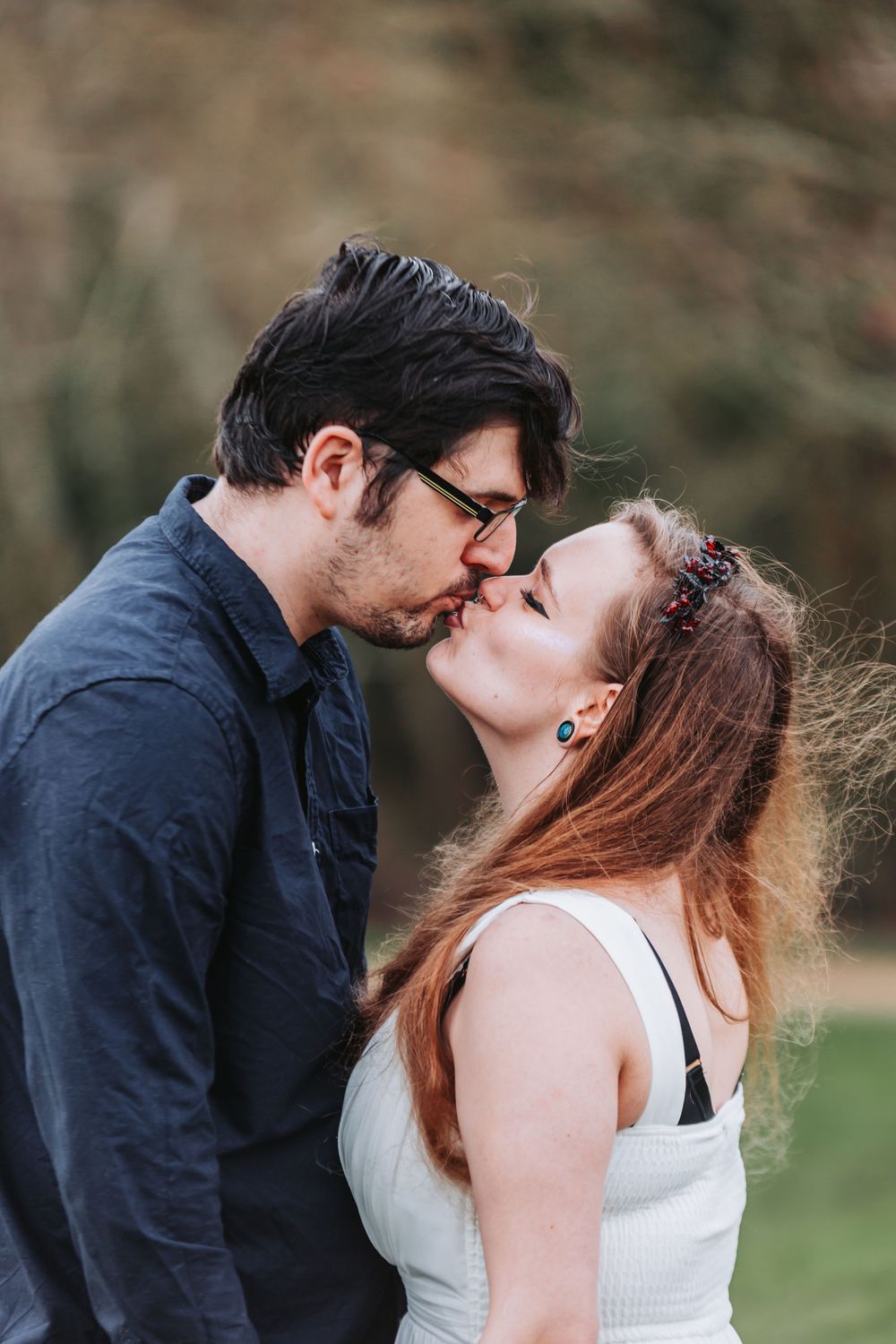 A romantic couple sharing a tender kiss outdoors with soft natural lighting and blurred background.