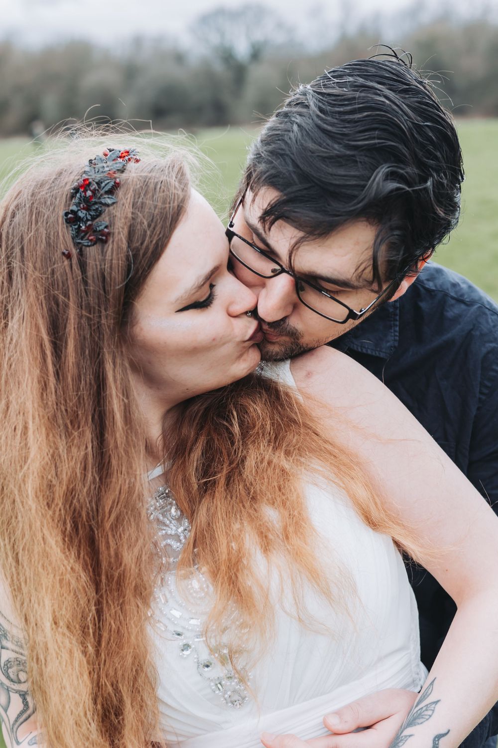 A romantic outdoor portrait of a couple sharing a tender kiss, with the bride wearing a white dress and floral headpiece.