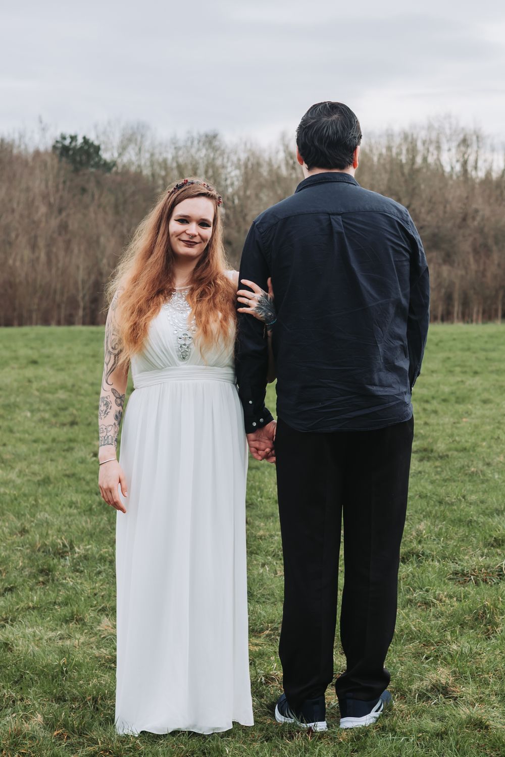 A couple stands together in a grassy field wearing white dress and black suit in a series of wedding photos.