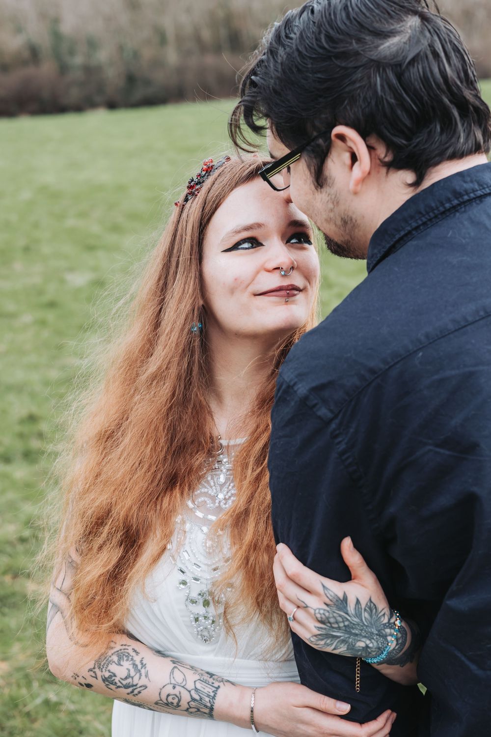 A couple in romantic poses outdoors, with the woman wearing a white lace dress and the man in black attire.