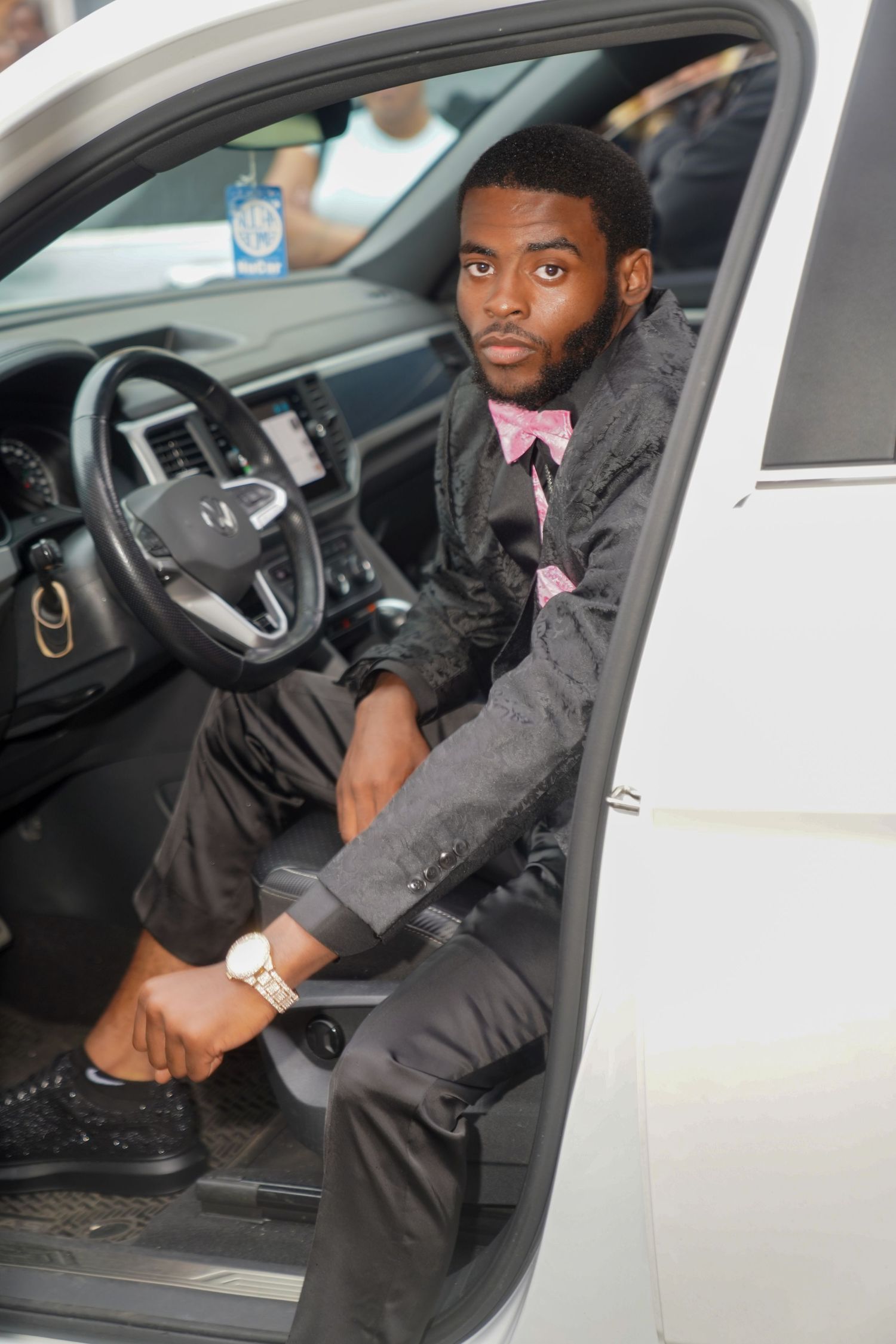 Four sequential photos show someone sitting in the driver's seat of a car wearing a black jacket and white watch.
