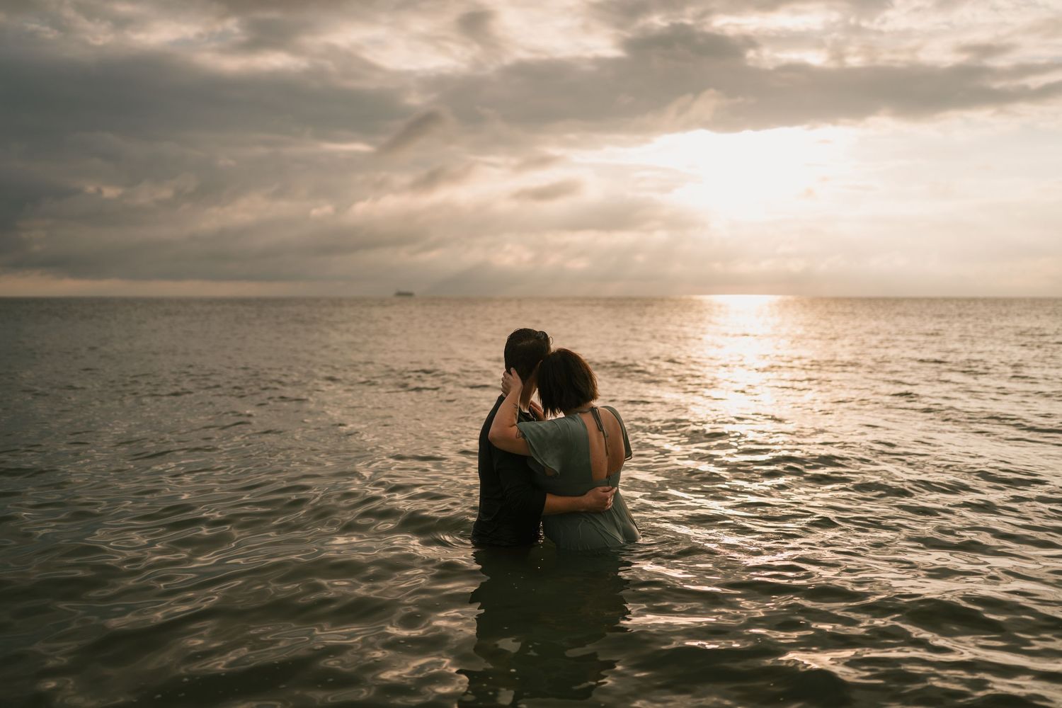 Silhouetted couple embrace in the ocean at sunrise in Cocoa Beach, Florida as waves ripple across the water. Intimate, moody session.