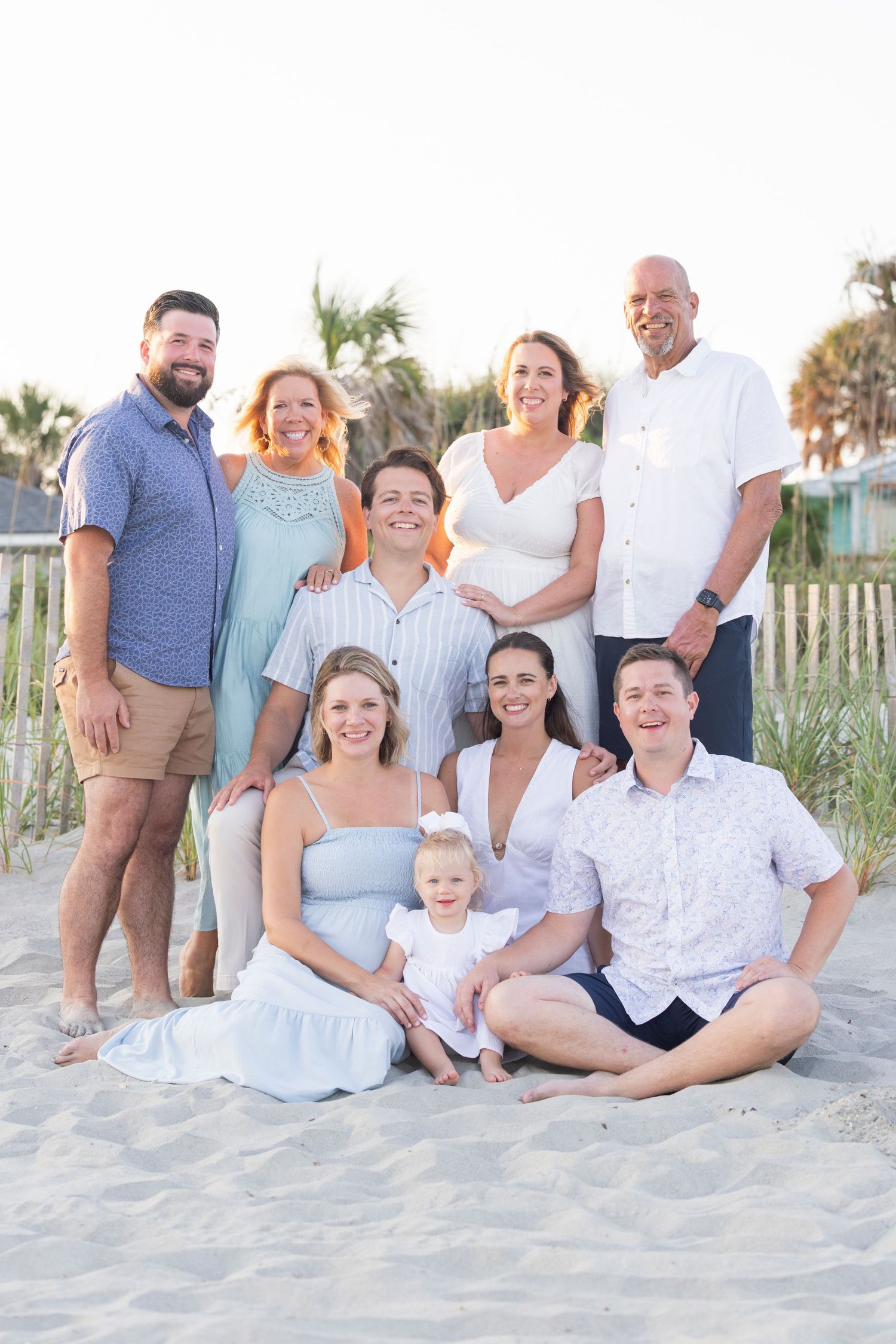 Large group photo of wedding guests posed under trees in blue and casual attire.