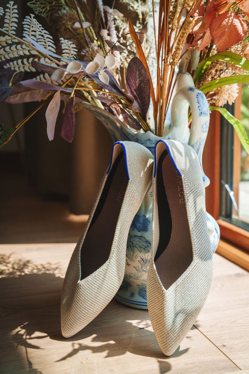 White bridal shoes sit on a windowsill with sunlight streaming in, creating dramatic shadows.
