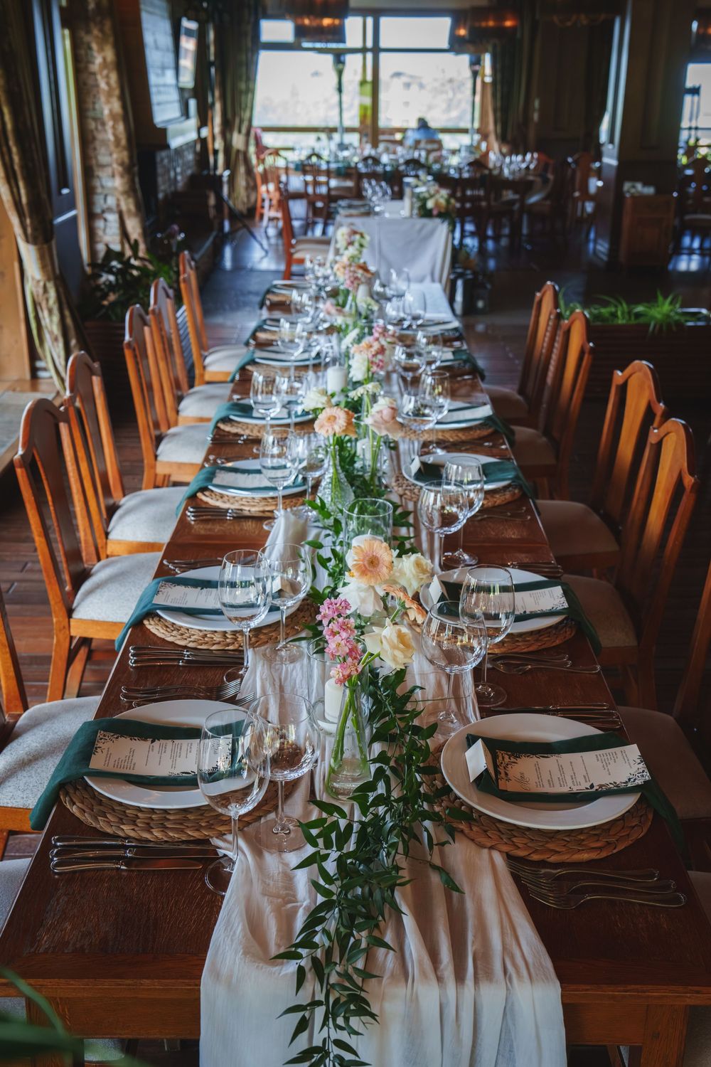Long wooden dining tables set with white linens, floral centerpieces and formal place settings in a rustic venue.