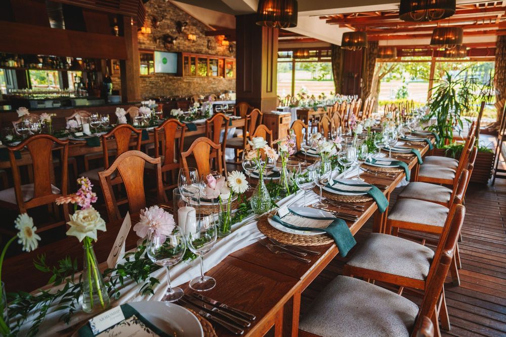 Panoramic view of a rustic wedding reception venue with wooden tables, string lights and natural decor elements.