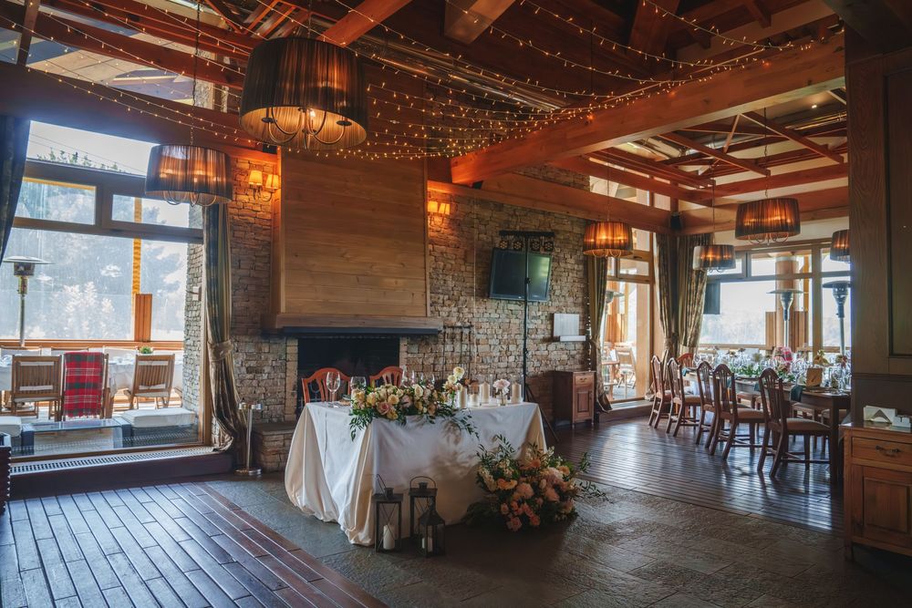 Rustic wedding reception venue with exposed wooden beams, stone walls, and elegant table settings in warm natural light.