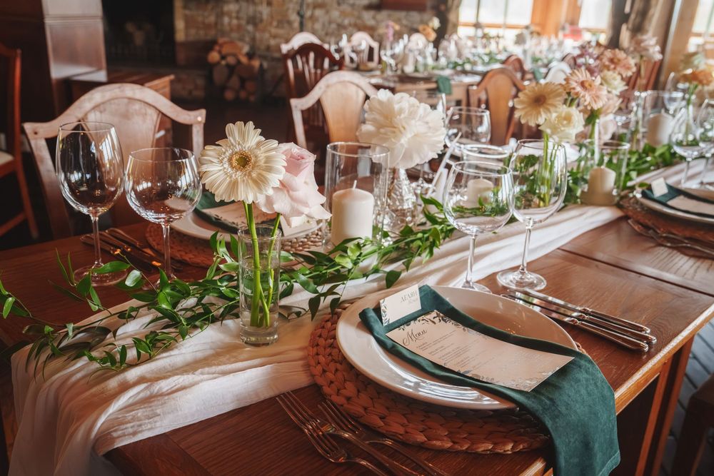 Elegant wedding table setting with white flowers, greenery garland, and teal napkins on a rustic wooden table.