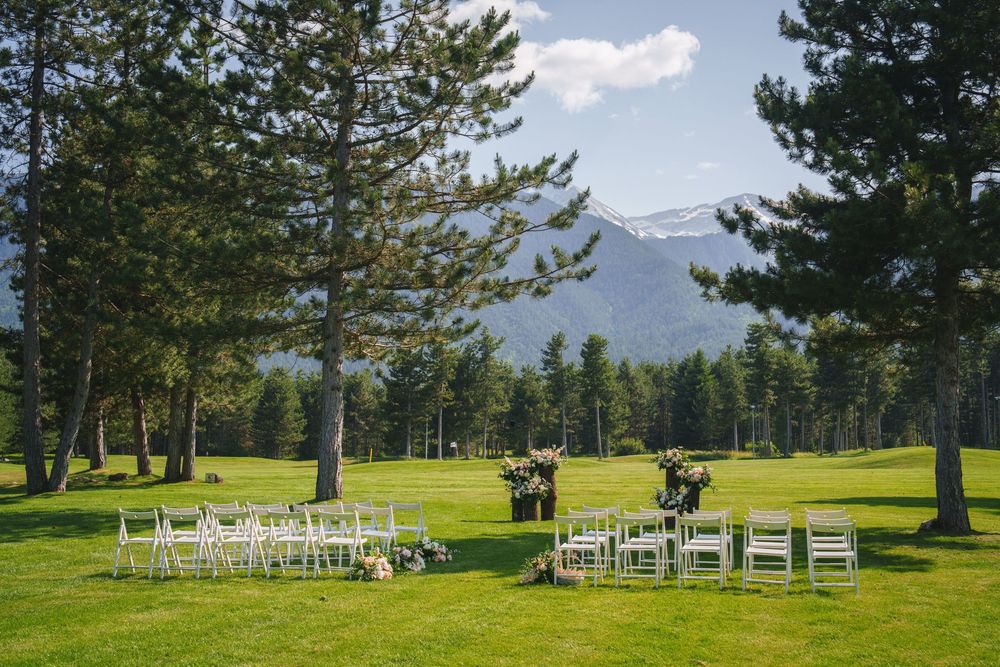 White chairs arranged for an outdoor wedding ceremony with mountain peaks and evergreen trees in the background.