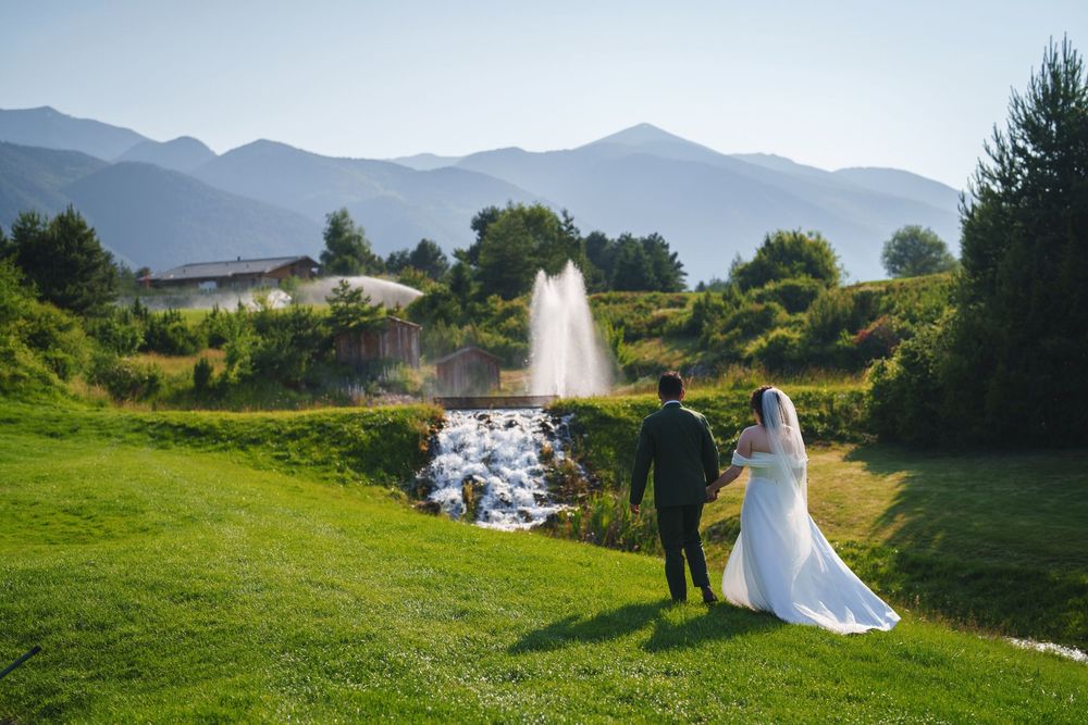 Wedding couple stands near a fountain on a golf course with mountain vistas in the background.