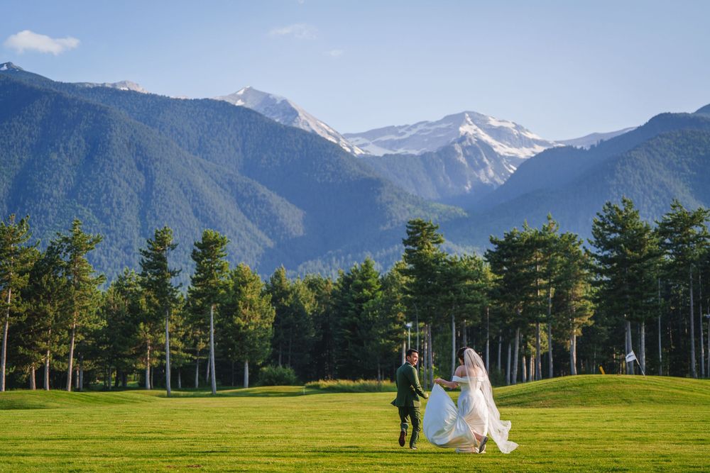 Panoramic view of a mountain wedding venue with snow-capped peaks and green meadow.
