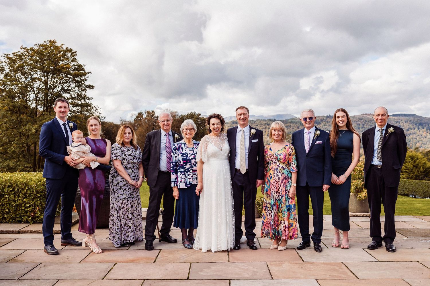 A group of wedding guests pose together outdoors on a cloudy day  in the Lake District for formal portraits.