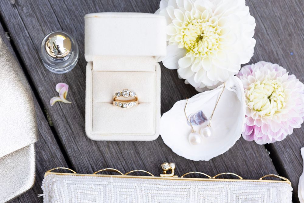 Wedding rings and floral decorations arranged on rustic wooden planks with soft pastel colors and white flowers.