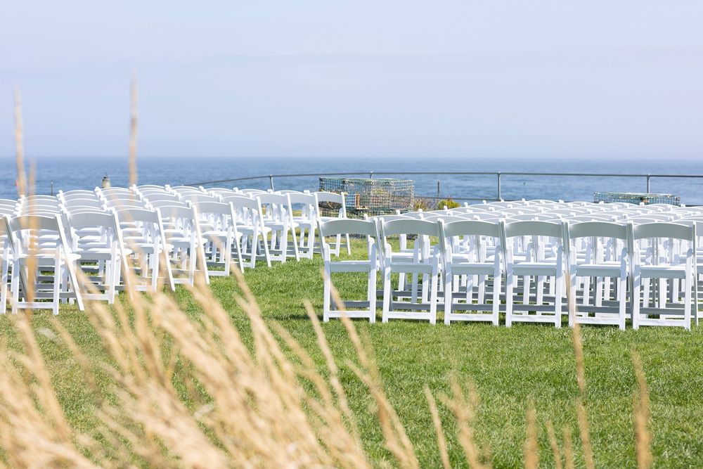 White chairs arranged in rows for an outdoor wedding ceremony overlooking the ocean on a grassy cliff.