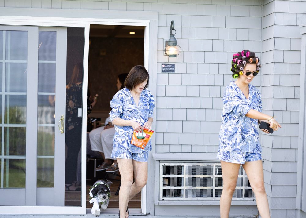 Two people wearing matching blue and white floral rompers exit a building with a small dog.
