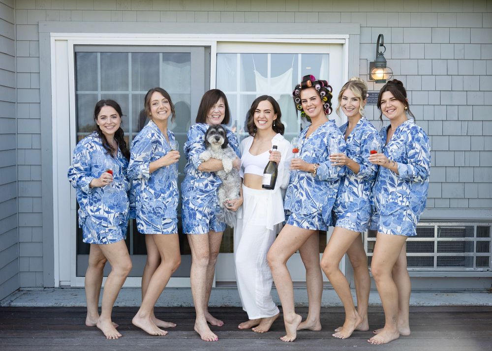 A group of women in matching blue and white floral dresses pose together on a porch.