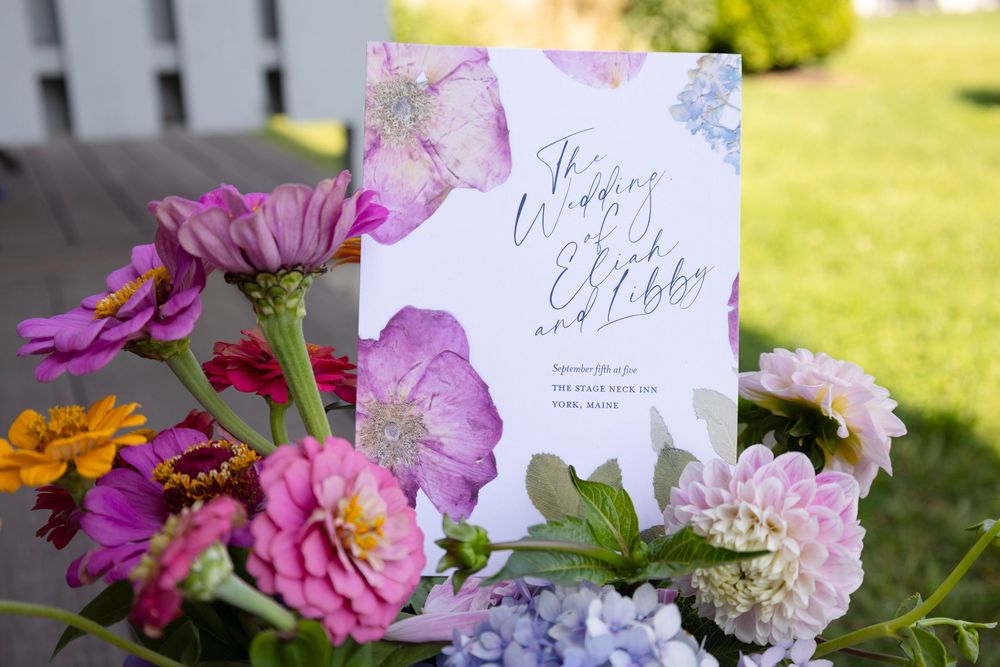 Colorful floral arrangements with pink and white flowers displayed outdoors on a sunny day with handwritten signs.