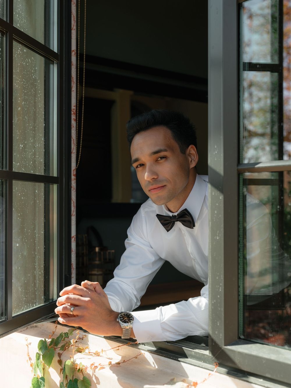 Person in formal attire leaning against a window frame in natural light.