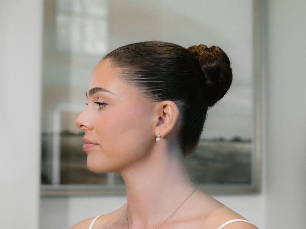 Woman with dark hair in a bun smiles while looking to the side in a bright indoor setting.