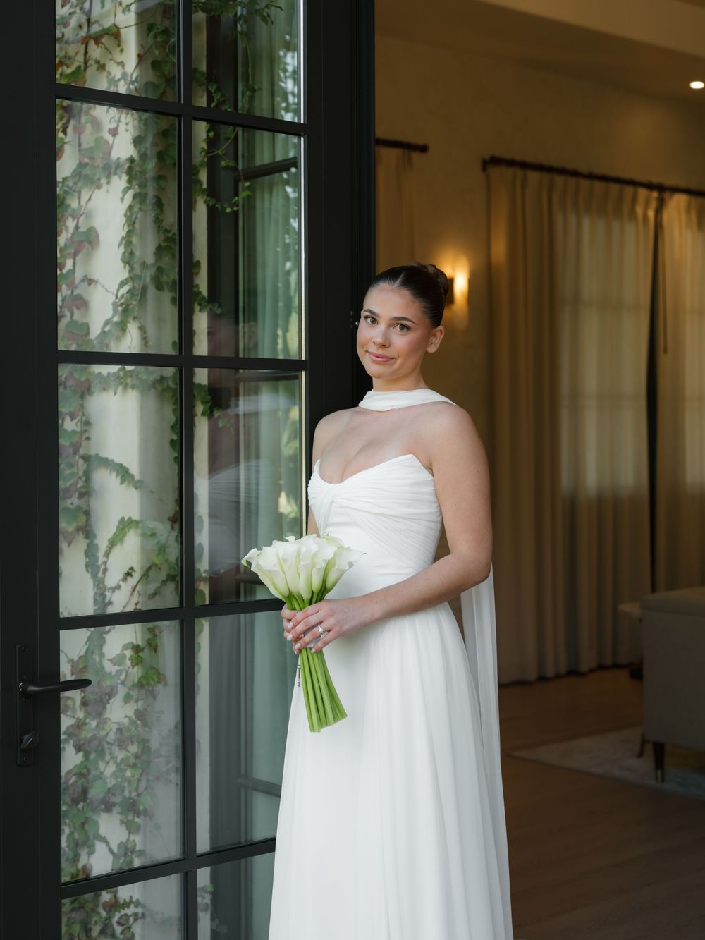A classic white wedding gown with sweetheart neckline and sheer overlay, complemented by a white calla lily bouquet.