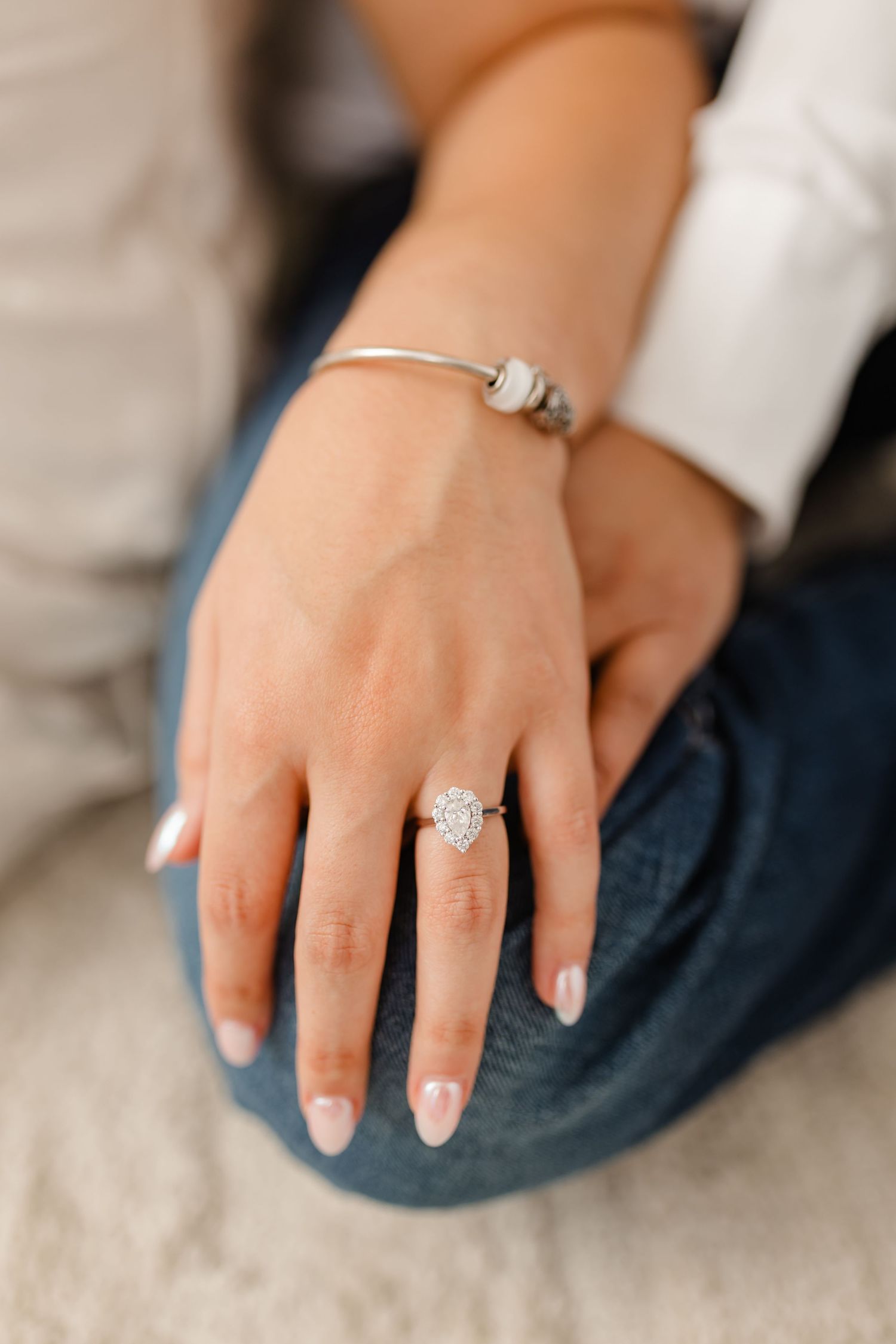 Close-up view of an elegant diamond engagement ring on a woman's hand with French manicured nails.