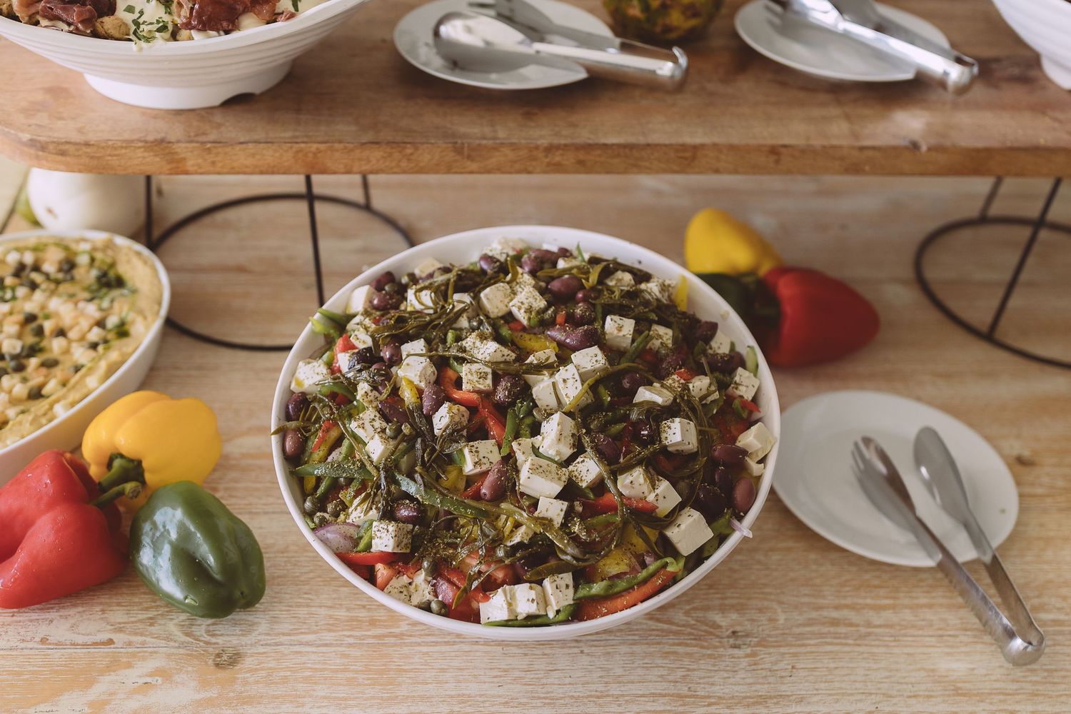 A Mediterranean bowl of food topped with feta cheese, tomatoes, and fresh herbs served on a rustic wooden table.
