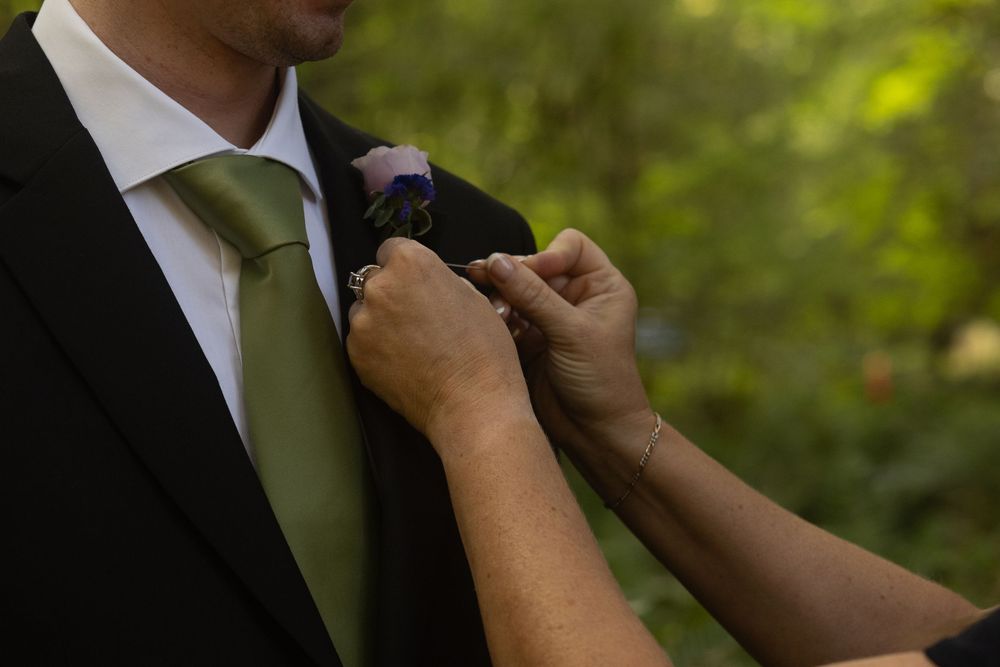 Hands adjusting green tie and suit details during wedding preparation.