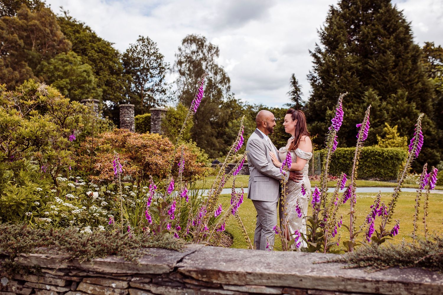 A couple embraces in a lush garden setting with vibrant purple foxgloves blooming in the foreground.