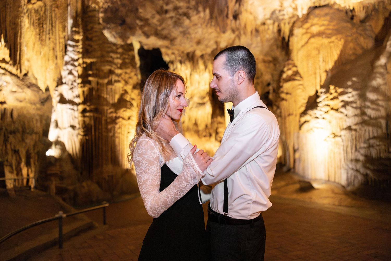 A couple shares a romantic moment in a dimly lit cave with stalactites hanging from above.