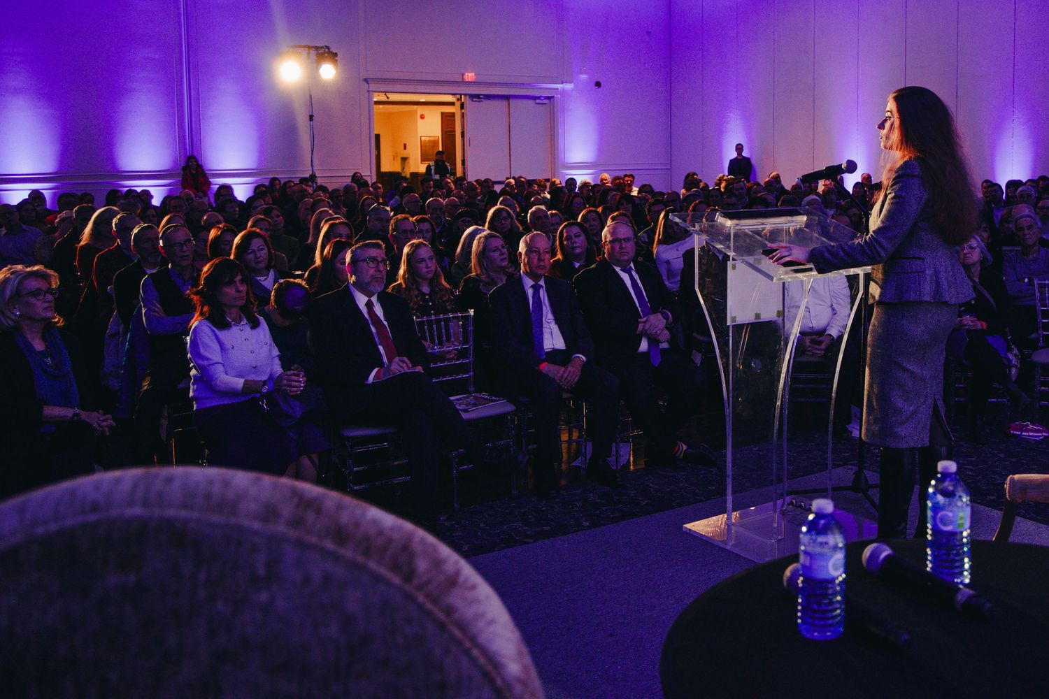 Musicians perform on stage at an event with purple lighting and a crowd visible in the background.